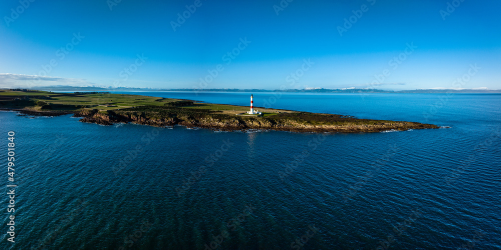an aerial view of tarbat ness lighthouse on easter ross in the highlands of scotland near inverness showing blue sky and calm seas with the lighthouse dominating the scene and rocks