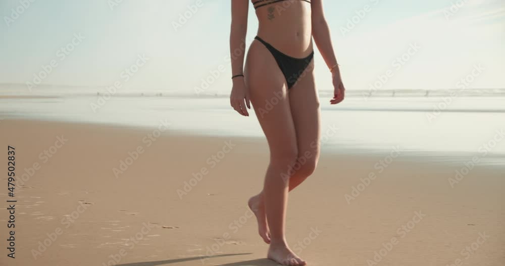 Caucasian fit young girl walking on the beach. Closeup woman legs walking in sand with black bikini bottom. Sunny day Caucasian fit young girl walking on the beach. Closeup woman legs walking in sand with black bikini bottom. Sunny day