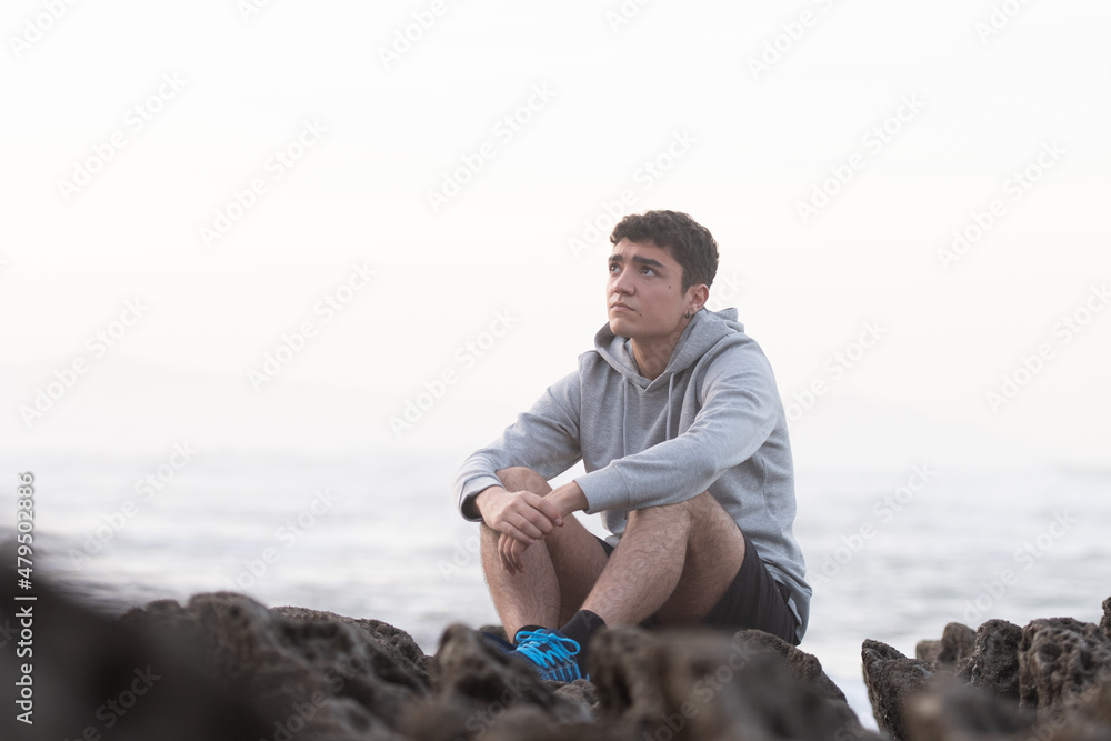 Thoughtful hispanic teenager sitting outdoors on rocks. Depression and anxiety in adolescence concept Thoughtful hispanic teenager sitting outdoors on rocks. Depression and anxiety in adolescence concept