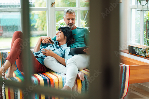 Man using tablet PC by woman seen through window at home