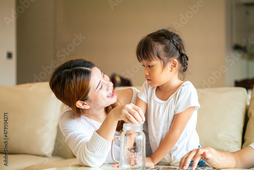 Asian mother teach their daughter to saving money and putting coins into glass bank spend a quality time together. Asian family, relationship, happiness and investment concept