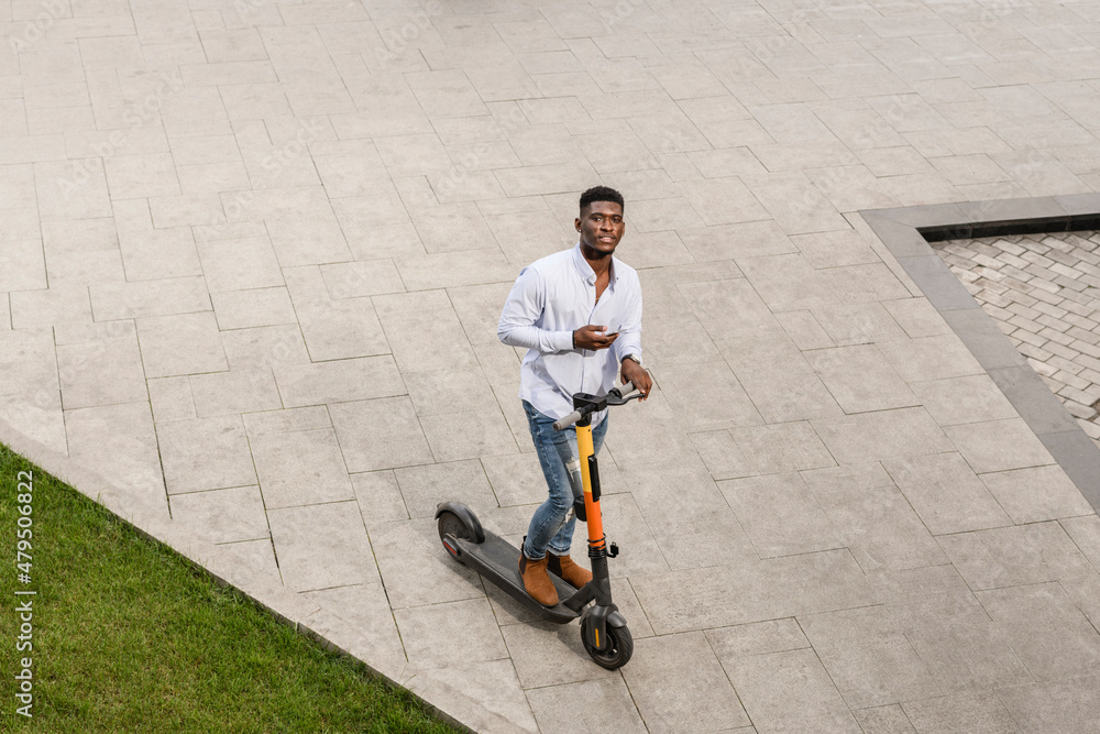 Young man with electric push scooter on footpath