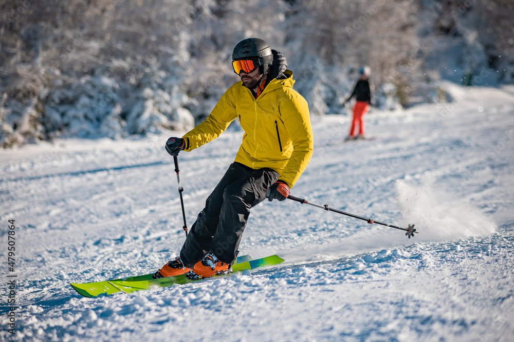 Young person in fashionable clothes is skiing past the camera on a ski slope on a sunny day. Carve or carving on ski piste, perfect weather, strong backlight.