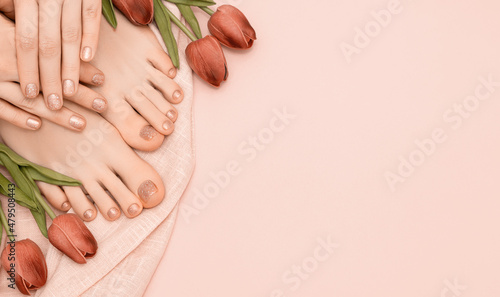 Female hands with spring nail design. Glitter beige nail polish pedicure. Female hands and feet with tulip flowers on pink background. Copy space.