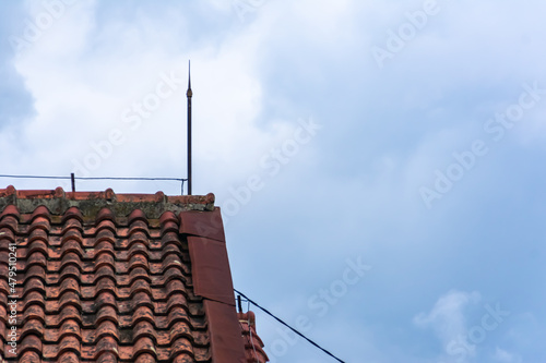 Fotografija house rooftile with the lightning rod stand upside under the bright blue sky