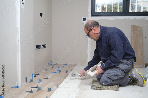 Senior tiler put tiles adhesive to the floor with the trowel and notched trowel.