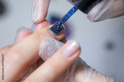the master of the nail service makes a manicure to apply a blue gel polish with a nail brush