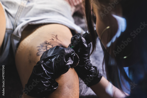 drawing of a tattoo on the leg close-up. Woman tattoo artist makes a drawing with a special machine in an art studio