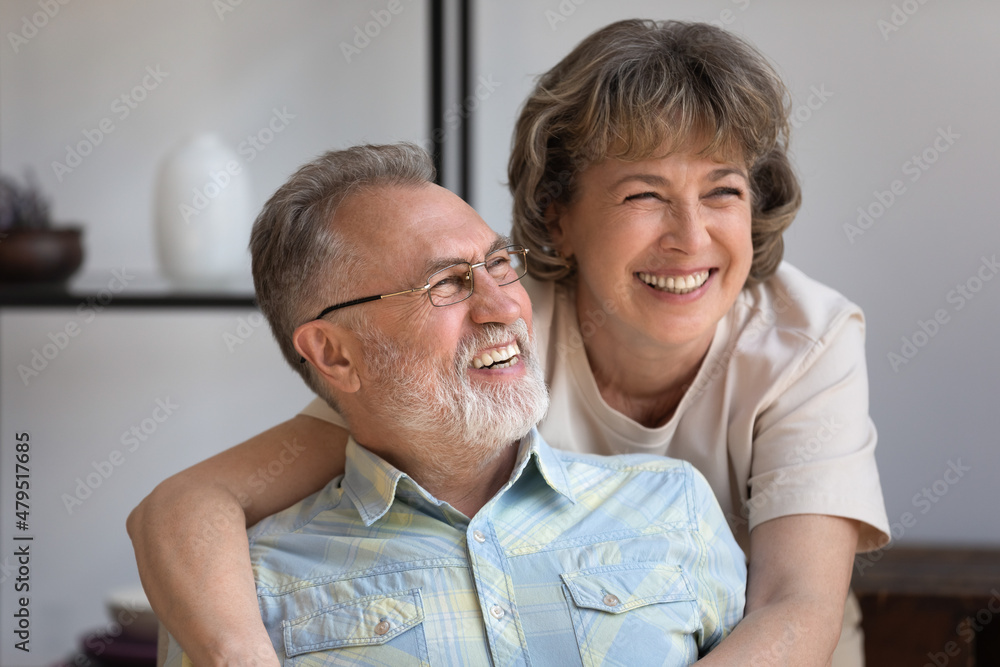 Head shot caring smiling middle aged woman cuddling happy older husband, laughing together at funny joke, looking in distance imagining future or enjoying pleasant conversation resting at home. Head shot caring smiling middle aged woman cuddling happy older husband, laughing together at funny joke, looking in distance imagining future or enjoying pleasant conversation resting at home.