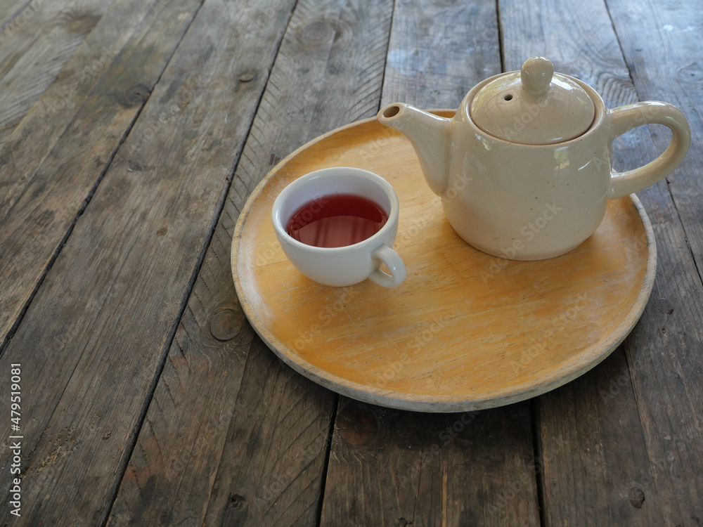 Red Color Tea Rose Petals in white cup and ceramic teapot on wooden tray on brown table Red Color Tea Rose Petals in white cup and ceramic teapot on wooden tray on brown table