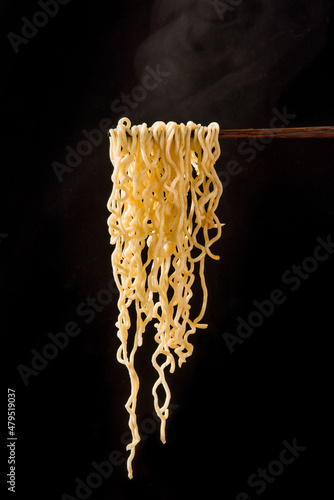 chopsticks with cooked instant noodles on black background photo