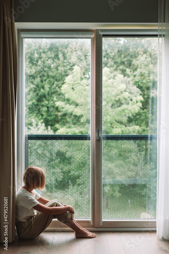 Depressed woman sitting on a floor looking through the window