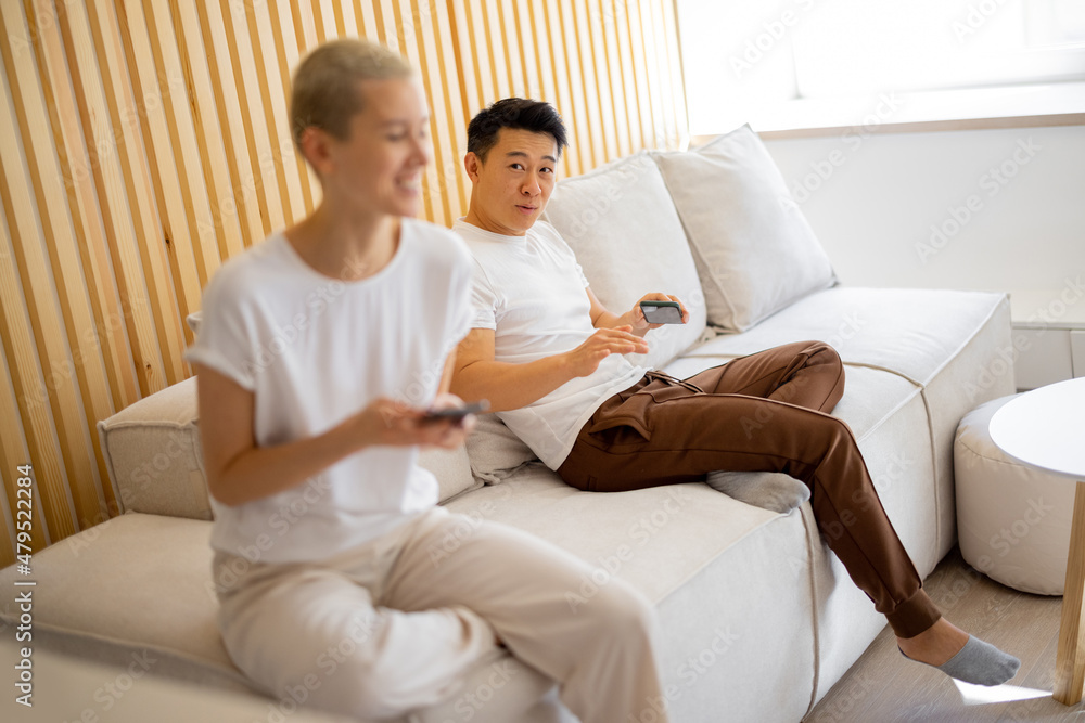 Multiracial couple having conflict while sitting on sofa at home. Concept of family relationship. Idea of domestic lifestyle. Disatisfied asian man looking on his serious caucasian girlfriend