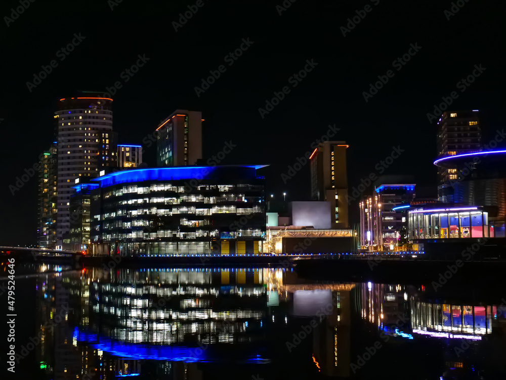 Fototapeta premium Vibrant reflections of modern buildings in Salford, Greater Manchester on calm dark water at night, copy space.