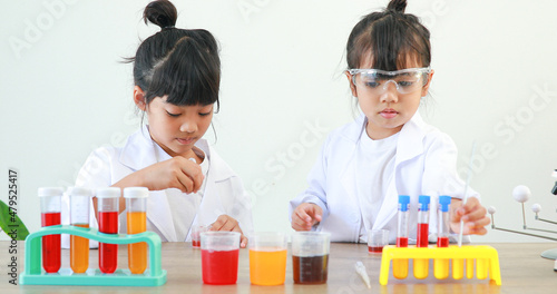 Little girl asian cute little student child learning research and doing a chemical experiment while making analyzing and mixing liquid in test tube at home on the table.