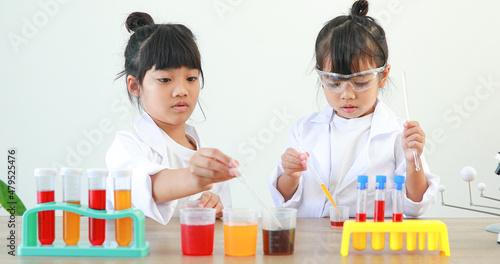 Little girl asian cute little student child learning research and doing a chemical experiment while making analyzing and mixing liquid in test tube at home on the table.