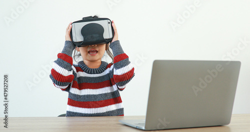 The little girl wearing VR sitting at desk in the home glasses virtual Global Internet connection metaverse. Future kids in white clothing wearing VR headsets for a game. concept advanced technology. © Narin Sapaisarn