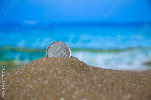 Russian coin, ruble in the sand on the background of beach and sea.