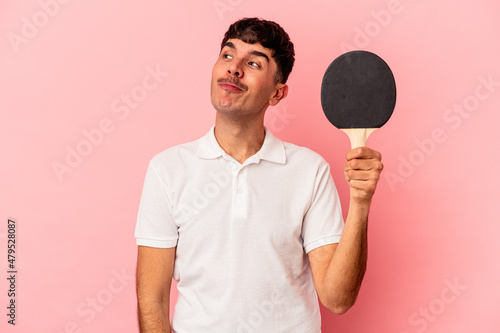 Young mixed race man holding a ping pong racket isolated on pink background dreaming of achieving goals and purposes