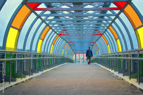 Man crosses the road over the bridge. Glass overhead passage through the highway. Bright multi-colored glass on a metal frame. New Moscow