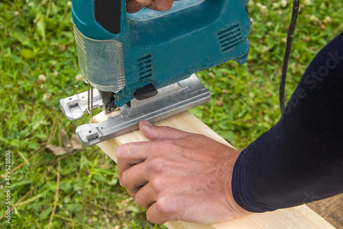 A man is sawing a board with a jigsaw. Work outdoors, hands do carpentry. Fretsaw in action