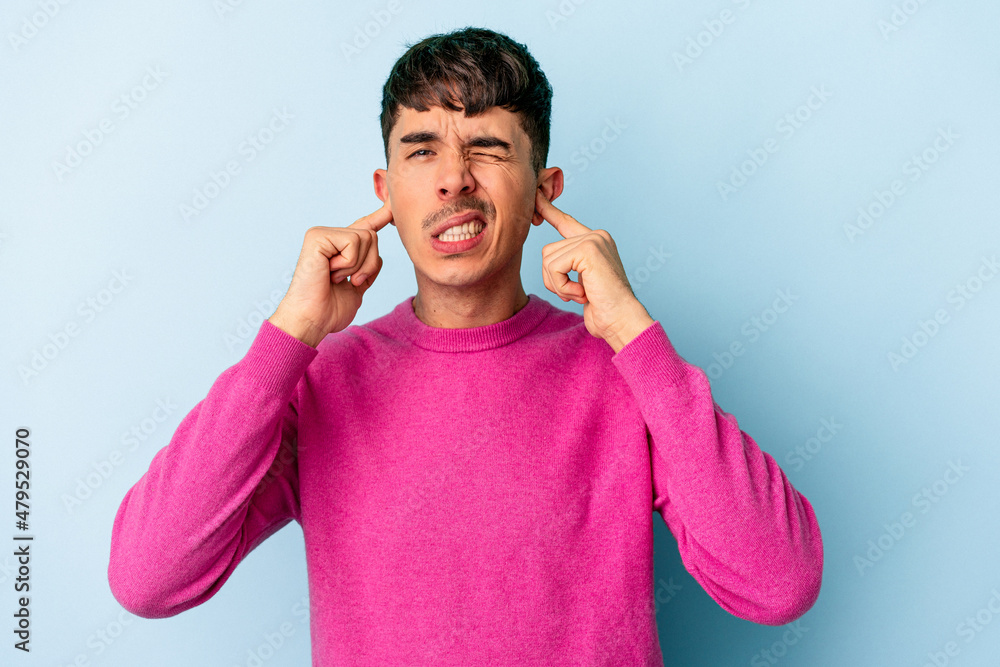 Young mixed race man isolated on blue background covering ears with fingers, stressed and desperate by a loudly ambient. Young mixed race man isolated on blue background covering ears with fingers, stressed and desperate by a loudly ambient.