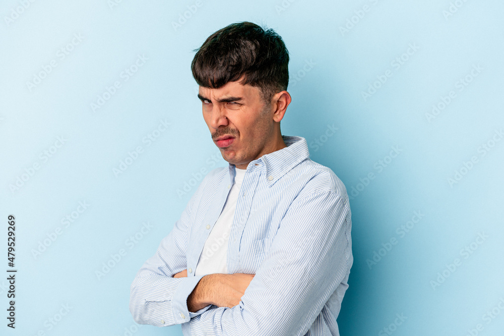 Young mixed race man isolated on blue background frowning face in displeasure, keeps arms folded. Young mixed race man isolated on blue background frowning face in displeasure, keeps arms folded.