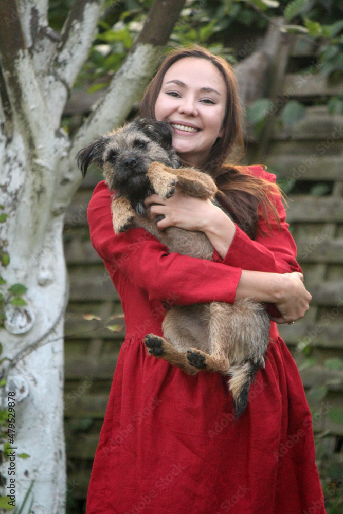 Close up portrait of smiling woman with cute furry dog in her hands. Female model in red dress with funny pet. Close up portrait of smiling woman with cute furry dog in her hands. Female model in red dress with funny pet.