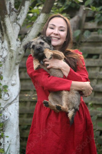 Close up portrait of smiling woman with cute furry dog in her hands. Female model in red dress with funny pet. 