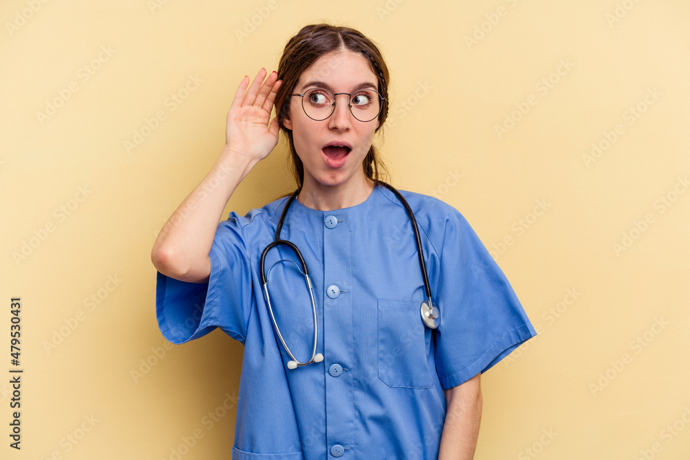 Young nurse caucasian woman isolated on yellow background trying to listening a gossip. Young nurse caucasian woman isolated on yellow background trying to listening a gossip.