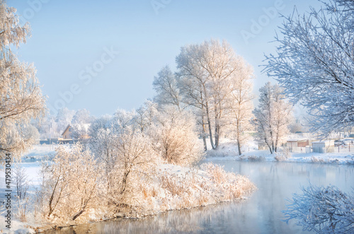Trees and a house in white snow frost on the river bank in the Moscow region on a winter sunny evening