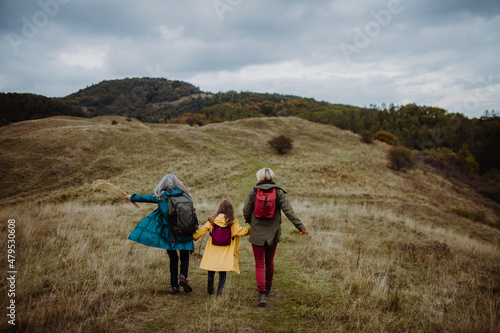 Rear view of small girl with mother and grandmother hiking outoors in autumn nature.