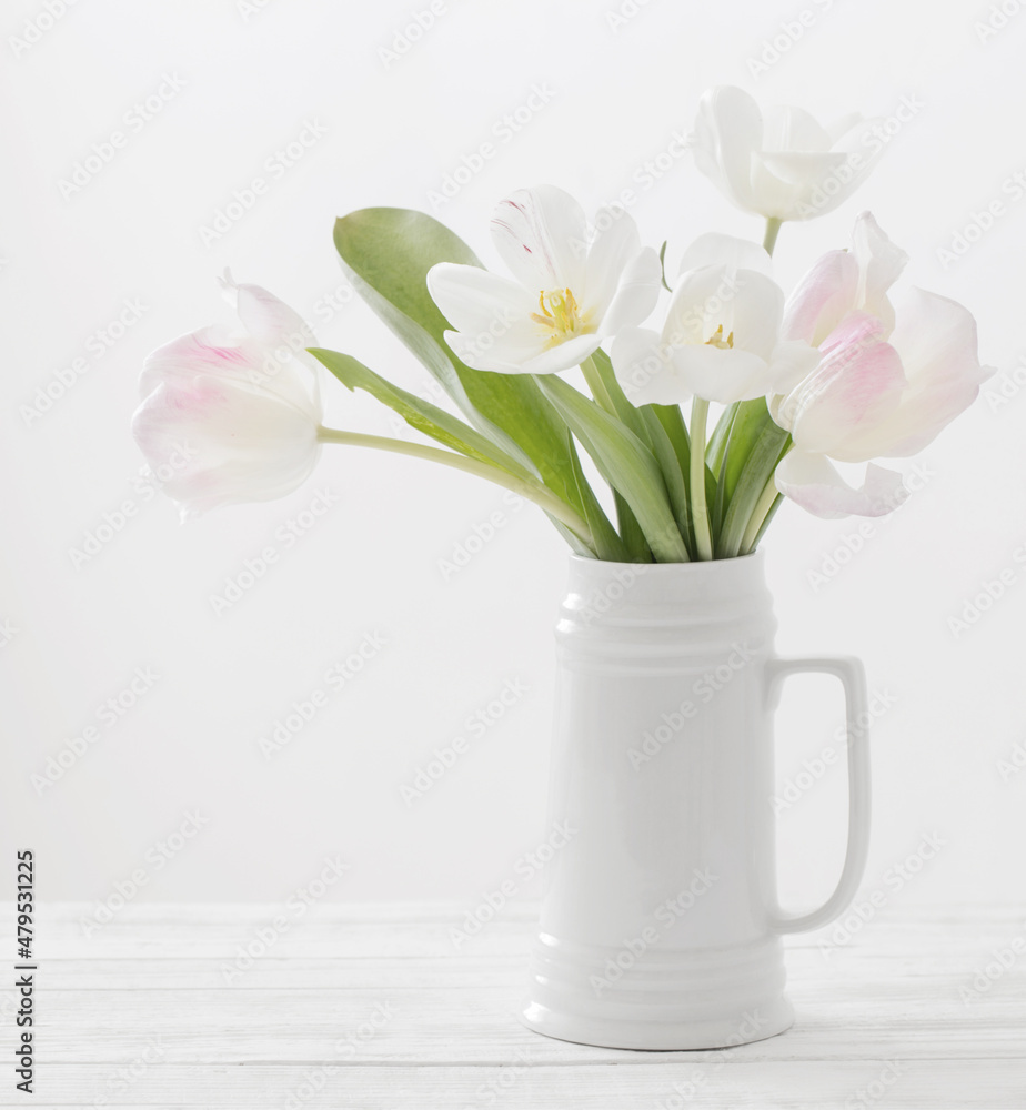 white and pink tulips in jug on white background