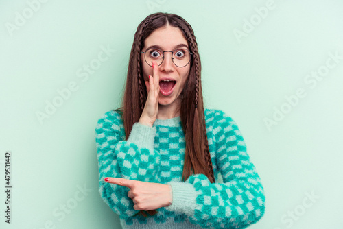 Young caucasian woman isolated on green background saying a gossip, pointing to side reporting something.