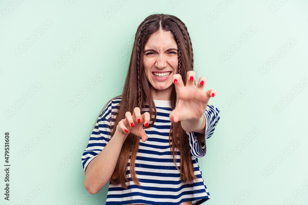 Young caucasian woman isolated on green background showing claws imitating a cat, aggressive gesture. Young caucasian woman isolated on green background showing claws imitating a cat, aggressive gesture.