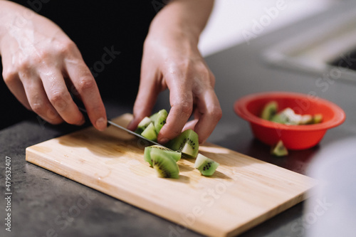 Woman cutting a kiwi. Hand with a knife cutting a kiwi on a wooden board