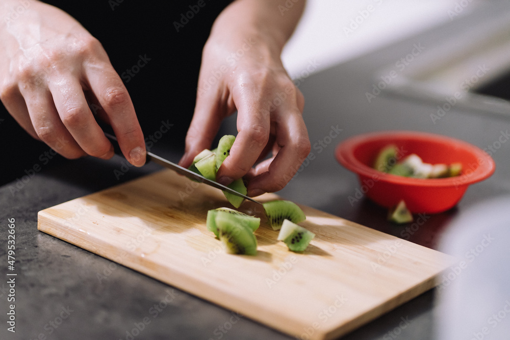 Woman cutting a kiwi. Hand with a knife cutting a kiwi on a wooden board