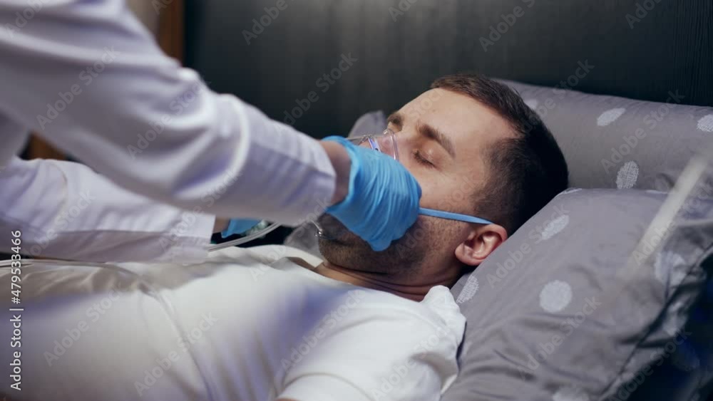 a doctor wearing personal protective equipment or PPE gives an oxygen mask to a European man with COVID-19 or coronavirus infection who has pneumonia in a hospital isolation ward. medical concept