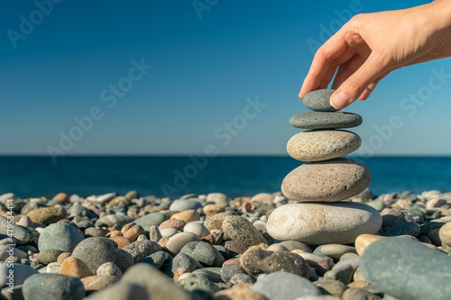 Canvas Print Close-up of a woman's hand putting the last stone on top of pebbles on the seashore on a sunny day, copy space