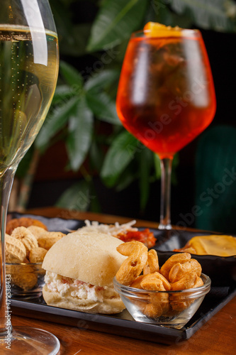 Aperitivo servito in un bar con prosecco e un cocktail di colore rosso come bevande e con arachidi, taralli, mini sandwich e finger food caldi come cibo