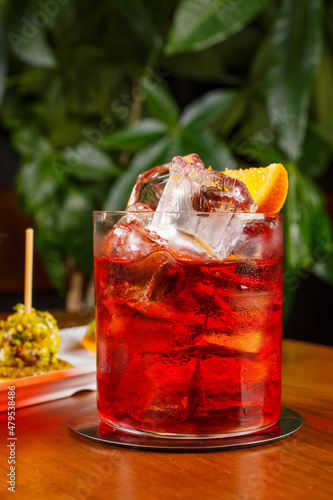 Cocktail rosso fatto con tequila infusa al caffè, Campari infuso al mango e Vermouth Carlo Alberto, poggiato su un tavolo di legno e accompagnato con finger food photo