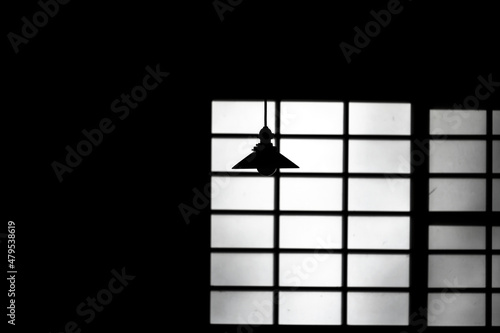 暗い部屋の格子の影の前に映る、天井からつり下がるランプ照明の影 photo