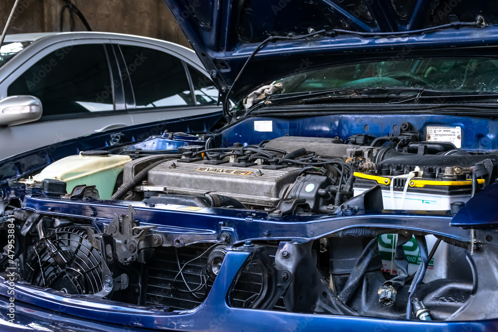 under repair blue car with many unmounted parts on the engine bay with the hood opened at the auto garage under repair blue car with many unmounted parts on the engine bay with the hood opened at the auto garage