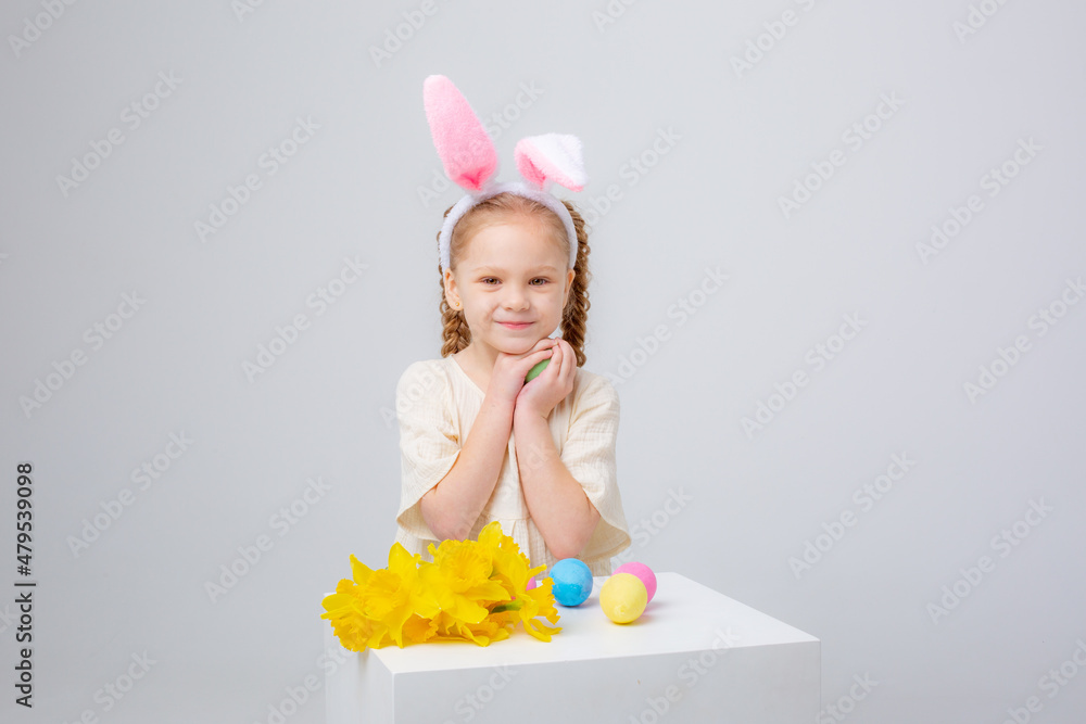 cute little girl with bunny ears on a white background with a basket of Easter eggs and flowers
