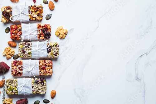 Energy granola bars with different seeds  nuts and dried fruits and berries on white marble background. Healthy snack concept.