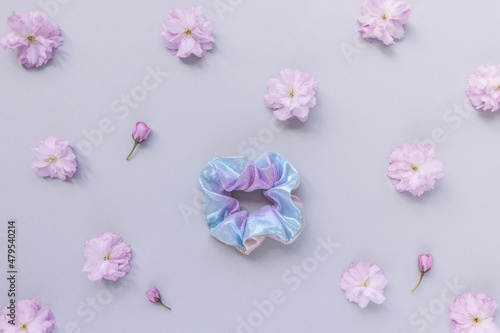 One shiny scrunchie and fresh spring cherry blossom pink flowers on pastel backround. Flat lay, top view. Diy accessories, hairstyle, lifestyle, spring outfit ideas concept, copy space