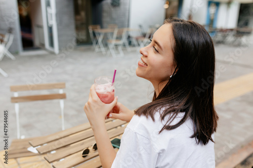 Close up portrait from back of adorable woman with brown hair drinking smoothie in open air terrace in warm day