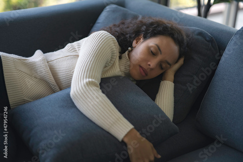 Lazy African American woman lying on the sofa. A young woman with sickness rests on the sofa inside the house. employees are stressed, causing headaches that are caused by over working.