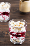 Homemade vegan dessert with meringues, coconut cream and cherries in glasses on a wooden table. Sugar, gluten and lactose free.