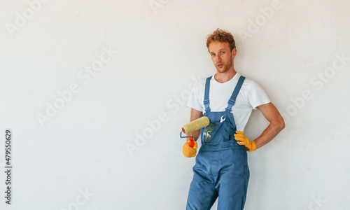 Standing against finished white walls. Young man working in uniform at construction at daytime